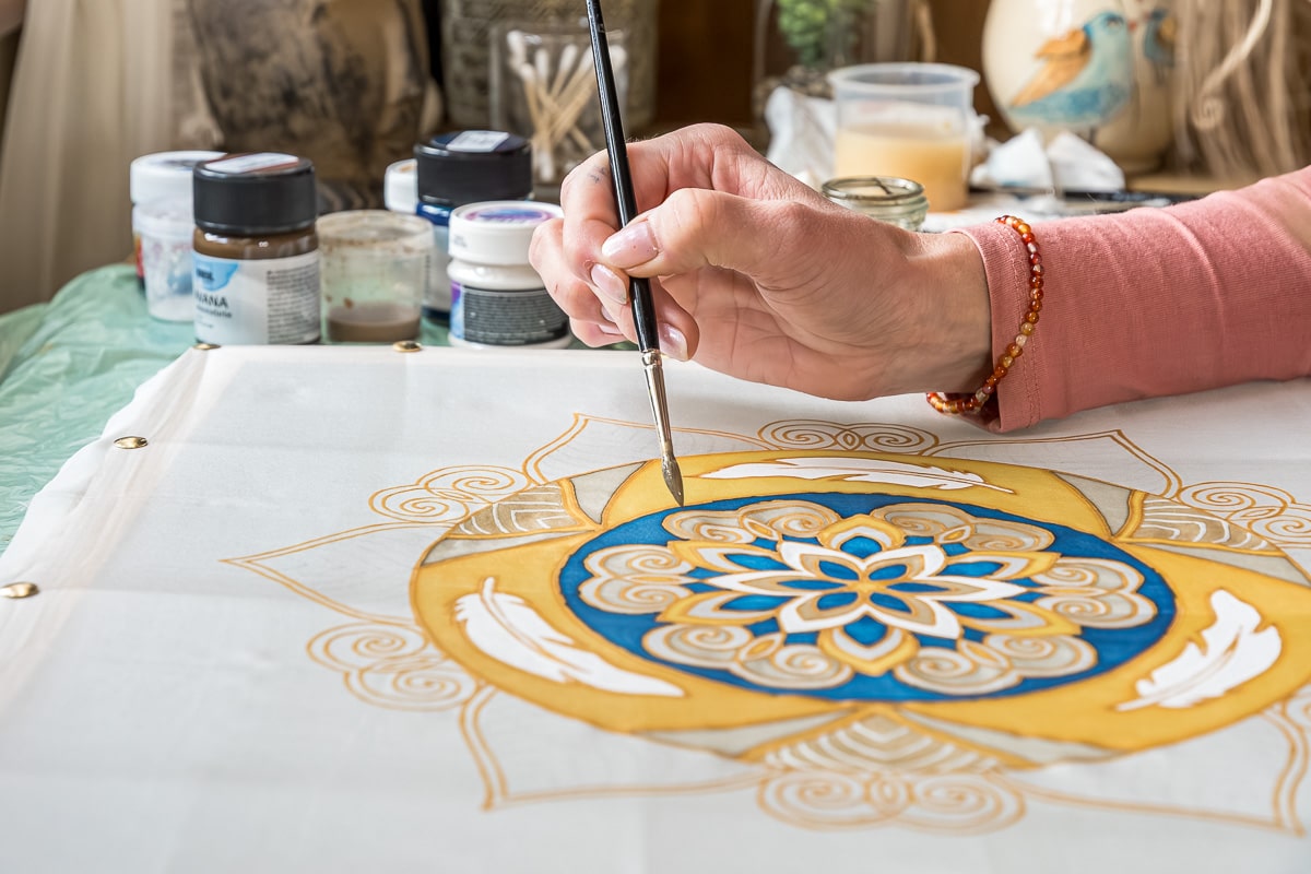 Ruka so štetcom pri maľovaní detailov mandaly na hodváb