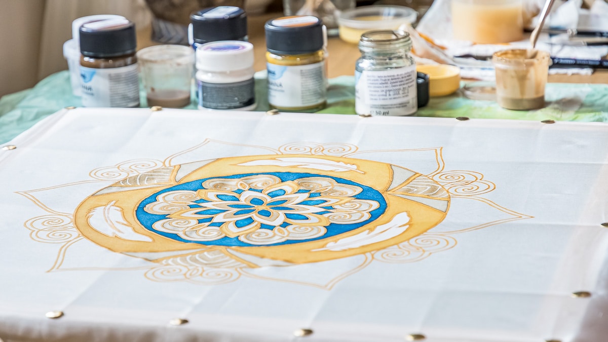 Mandala na hodvábe počas maľby, obklopená farbami a štetcami