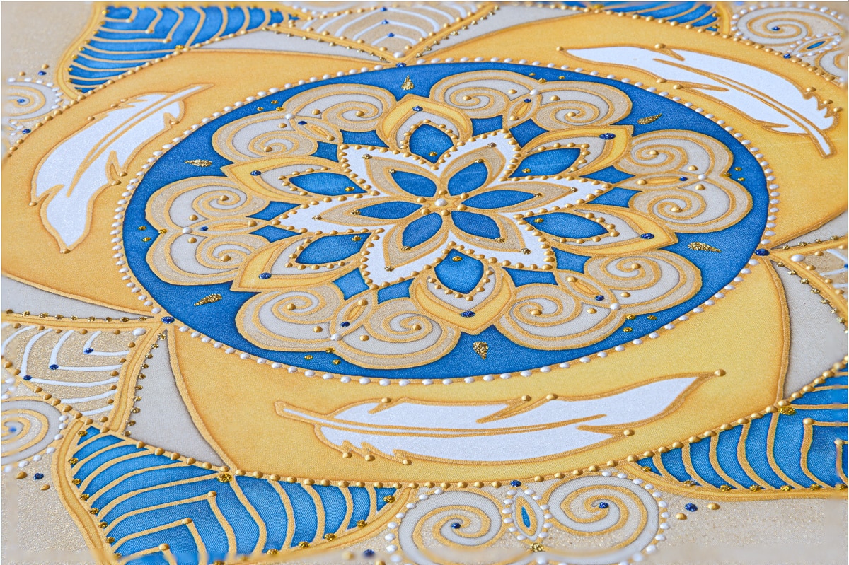 Detail hotovej zlatej a modrej mandaly s perím a ornamentmi