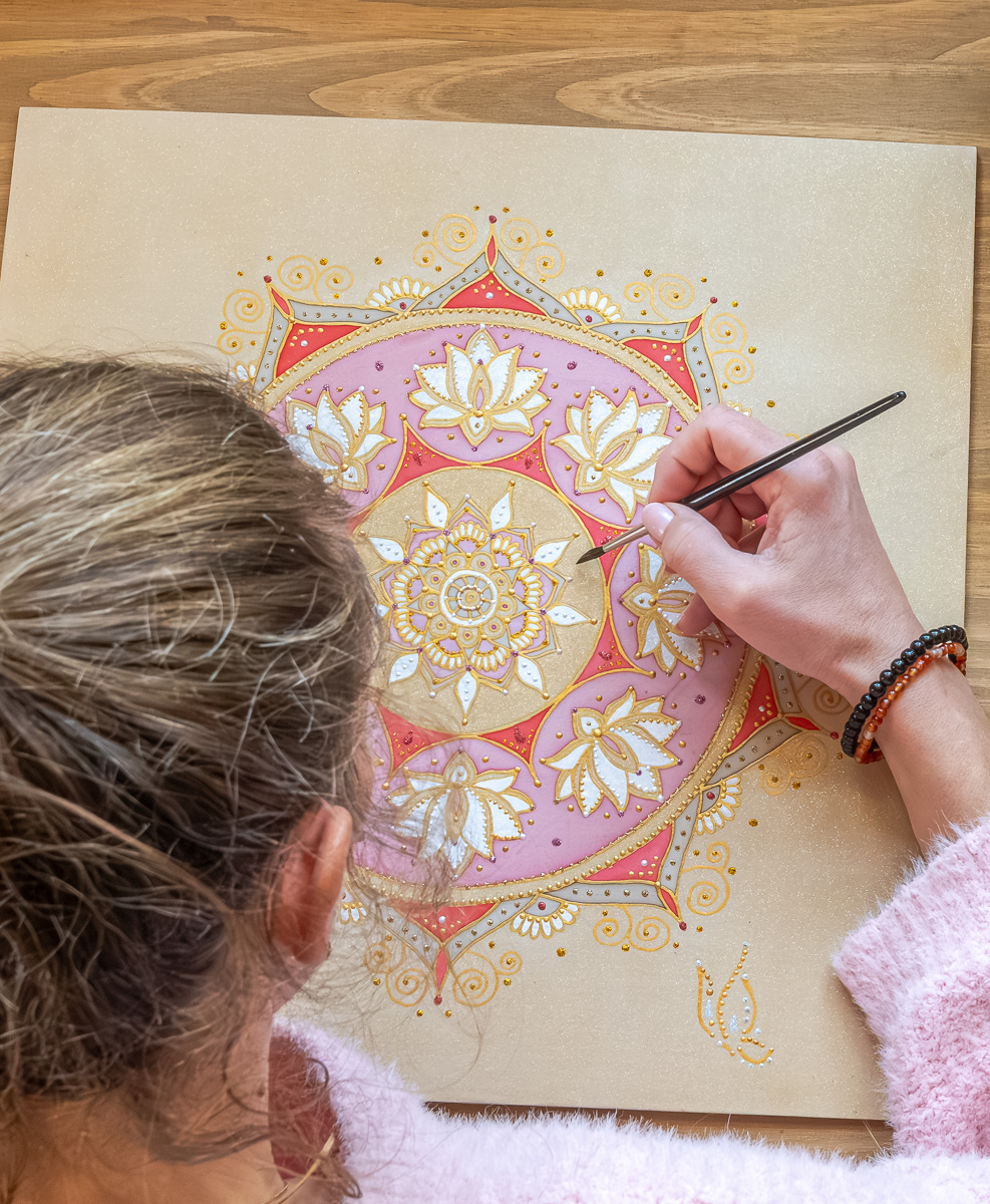 Ruka maľuje osobnú mandalu na hodváb, okolo farby a štetce